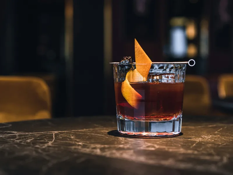 Een cocktail met sinaasappelschil op een donkere marmeren bar