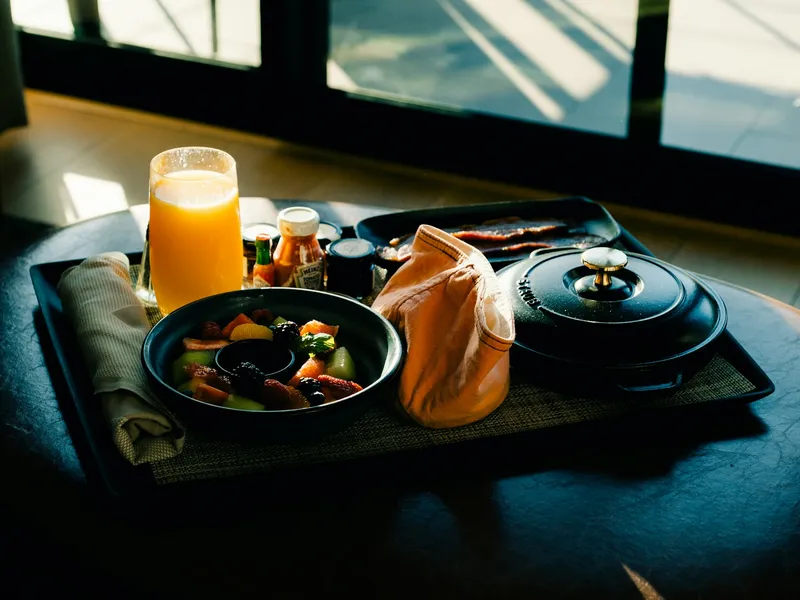 Een ontbijtdienblad bij het raam in ochtendlicht: sap, fruit, een gietijzeren pannetje