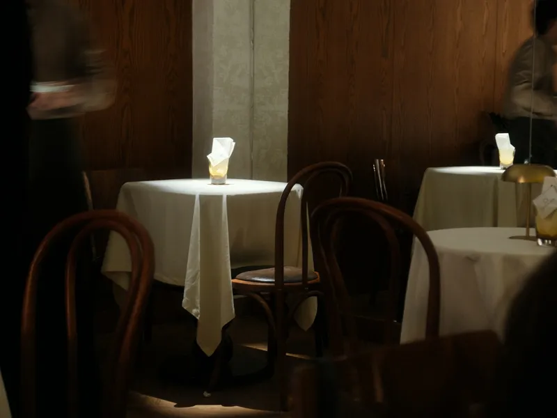 Een restaurant in de avond: tafels met wit linnen en een kaars, houten stoelen