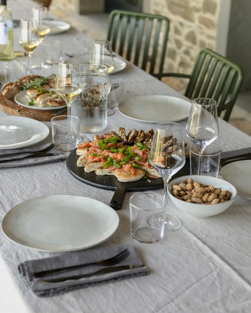 Een gedekte tafel in een villa van Rouchelli, met wijnglazen en borden op wit linnen